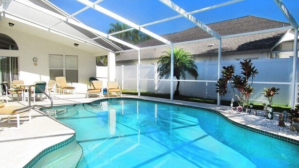 A swimming pool with a sunshade, lounge chairs, and a palm tree. - Family Fun 4 bedroom Vacation home (Kissimmee)