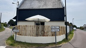 Un edificio con tetto scuro e facciata bianca, caratterizzato da un recinto in legno e un ombrellone bianco. Sono presenti segnali direzionali che indicano 'Le Pont' e 'La Haule'.