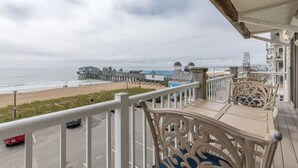 Een balkon met gedetailleerde witte hekwerken met uitzicht op een strand en een pier.