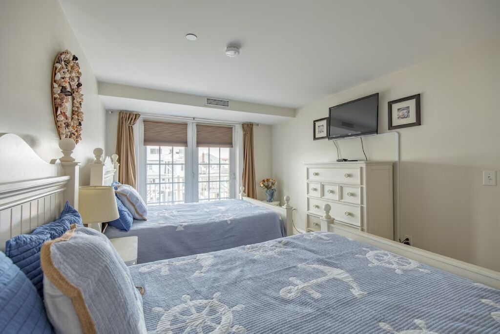 A hotel room with two beds, a TV, a dresser, and a window with curtains.