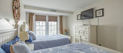 A hotel room with two beds, a TV, a dresser, and a window with curtains.