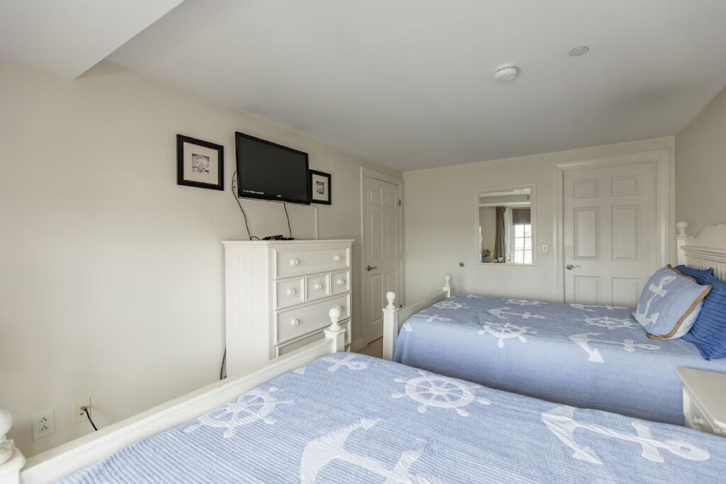 A bedroom with two beds, a dresser, a television, and a mirror.