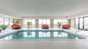 An indoor swimming pool with three red cushioned seating areas and large windows offering views of the city. - Direct Ocean Front Unit With Private Balcony. (Old Orchard Beach)