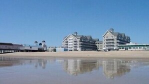 A beachfront hotel with multiple buildings, a pier, and calm water reflecting the structures. - Direct Ocean Front Unit With Private Balcony. (Old Orchard Beach)