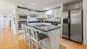 A modern kitchen with white cabinetry, stainless steel appliances, and a central island with bar stools. - Direct Ocean Front Unit With Private Balcony. (Old Orchard Beach)