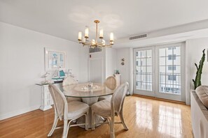 A dining area with a round glass table, wicker chairs, a chandelier, and a view through large windows. - Direct Ocean Front Unit With Private Balcony. (Old Orchard Beach)