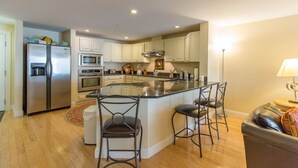 Een moderne keuken met een centraal eiland, roestvrijstalen apparatuur en een zithoek met barstoelen.