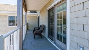 A covered balcony with wooden chairs, a sliding glass door, and a brick wall.