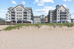 Een strandhotel met meerdere balkons, een restaurant aan het strand en een zandstrand op de voorgrond.