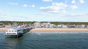 Une ville côtière dotée d’une jetée qui s’avance dans l’eau, avec un grand bâtiment à multiples balcons et une grande roue en arrière-plan.