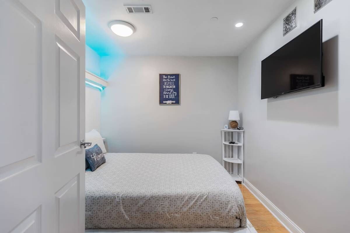 A bedroom with a bed, a TV mounted on the wall, and a shelf with items.
