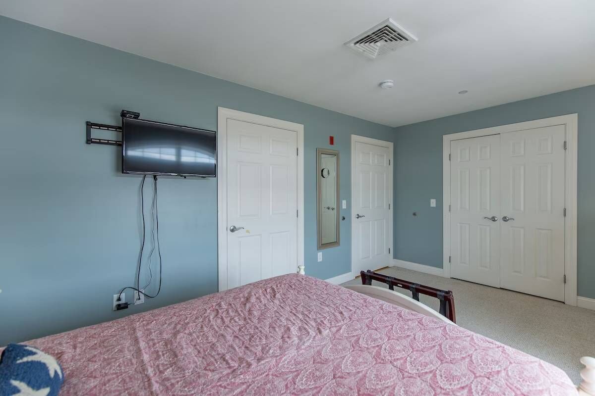 A bedroom with a bed, a flat-screen TV mounted on the wall, and two white doors.