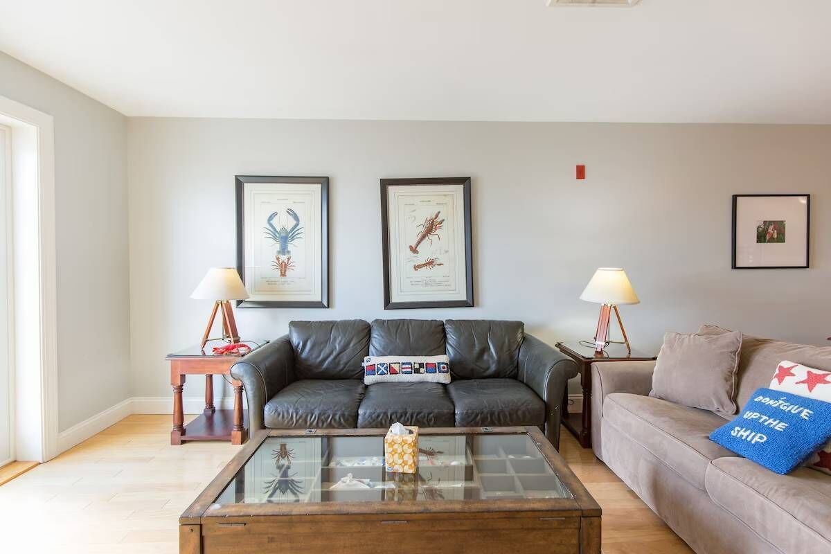 A living room with a leather sofa, a glass coffee table, and two framed botanical prints on the wall.