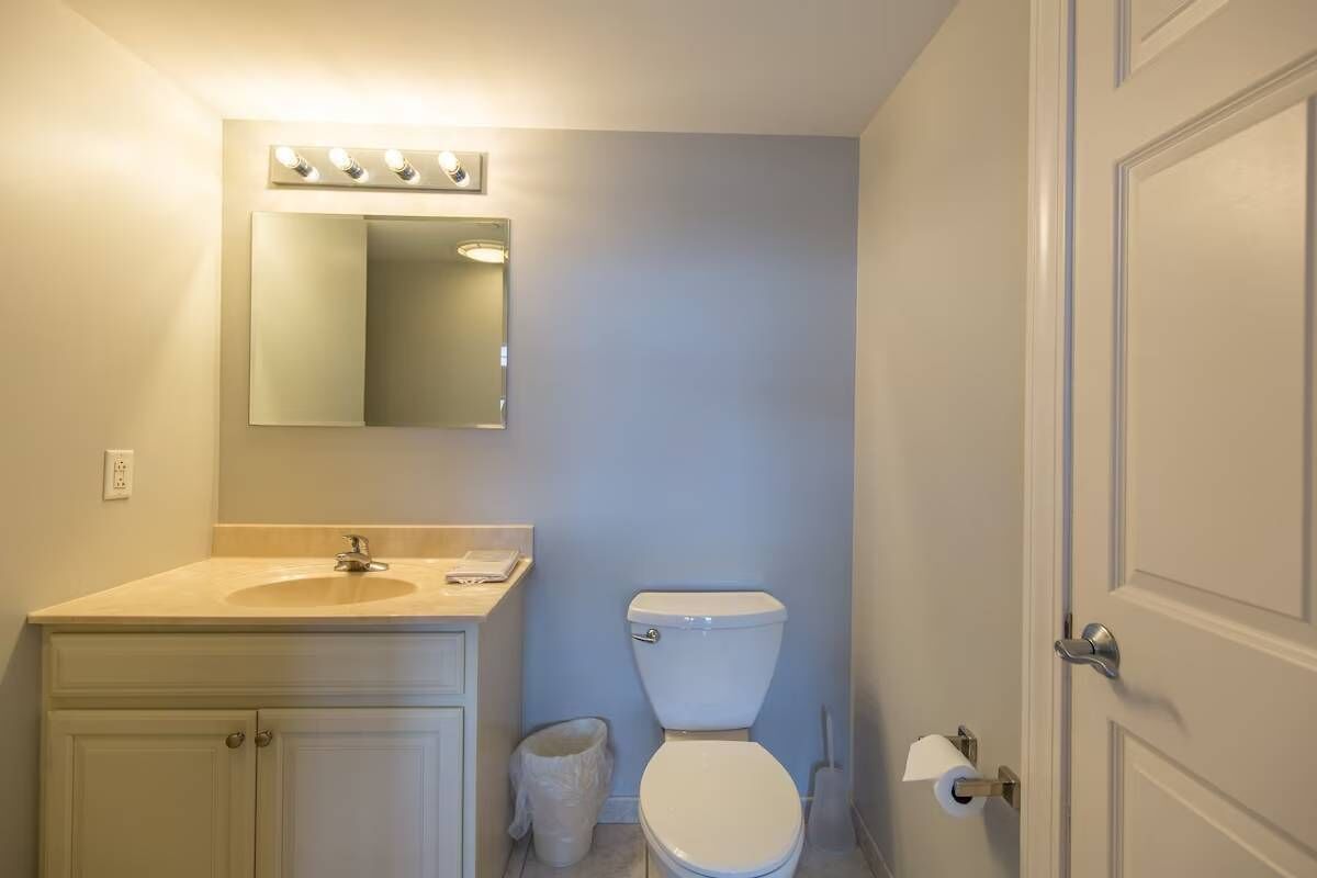 Een badkamer met een wastafel, spiegel, toilet en een prullenbak.