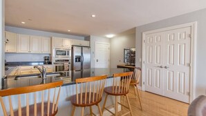 A modern kitchen with white cabinets, stainless steel appliances, and wooden bar stools. - Grand Victorian unit 511 (Old Orchard Beach)