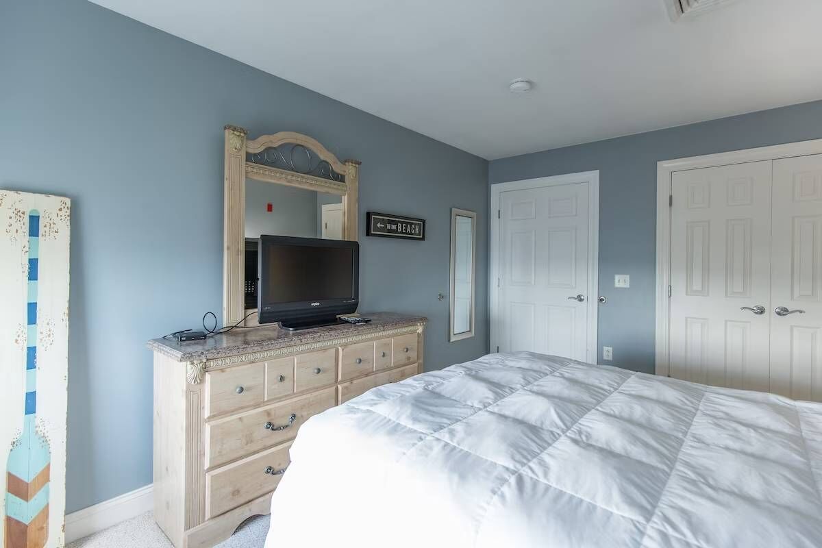 Un dormitorio con cama, cómoda, televisor y un cartel que indica la dirección a la playa.