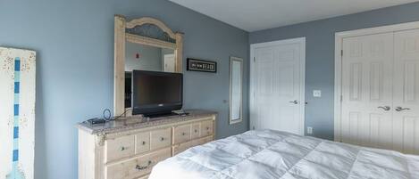 A bedroom with a bed, dresser, TV, and a sign indicating a beach direction.