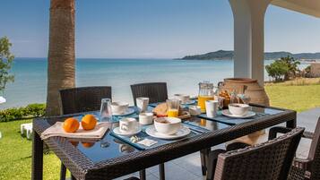A breakfast table set with white dishes, orange fruits, and a pitcher of orange juice, overlooking a scenic coastal view.