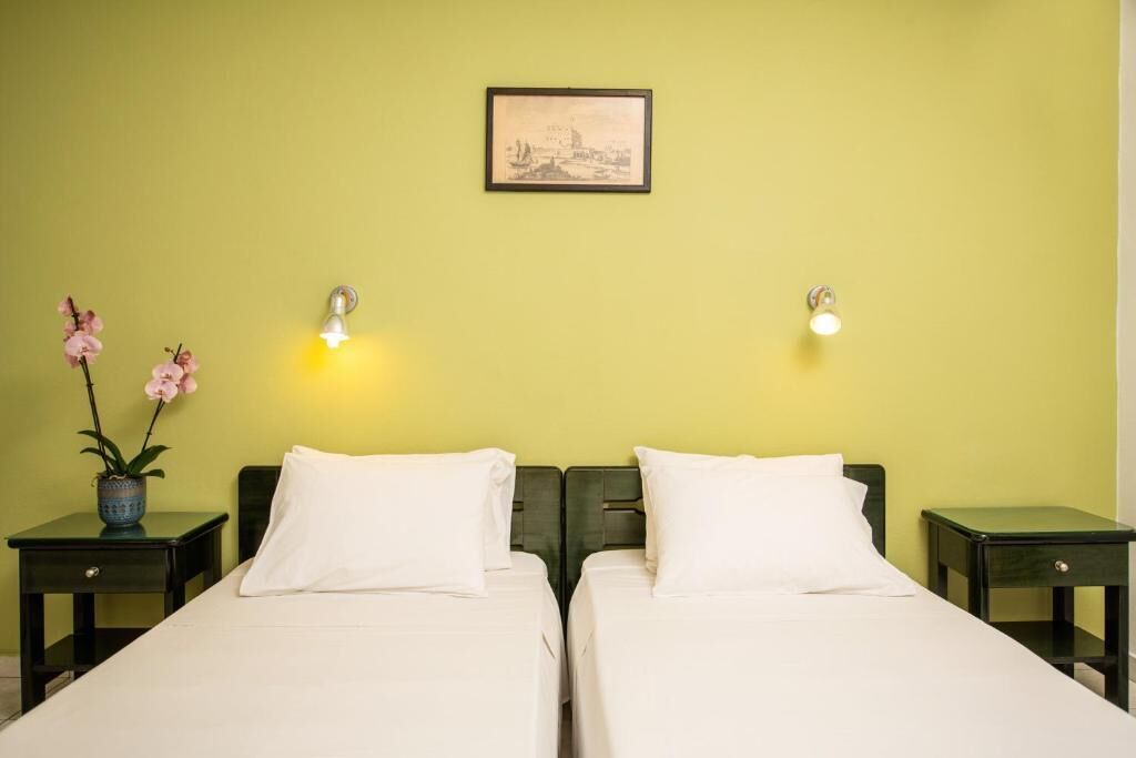 Una habitación con dos camas, un cuadro en la pared y un florero con flores sobre una mesita de noche.