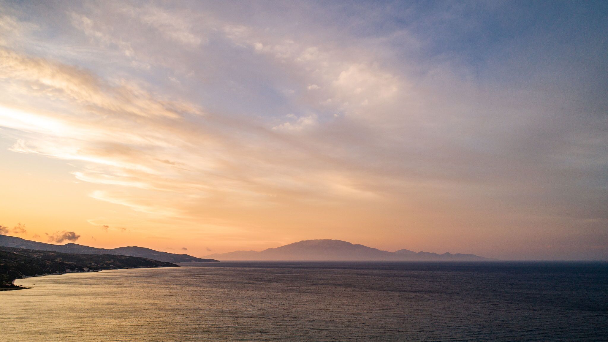 Un paysage côtier avec une mer calme, des montagnes lointaines et un ciel dégagé.