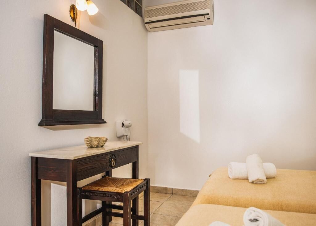 A hotel room with a dark wooden desk, a mirror, an air conditioner, a bed with towels, and a small decorative item on the desk.