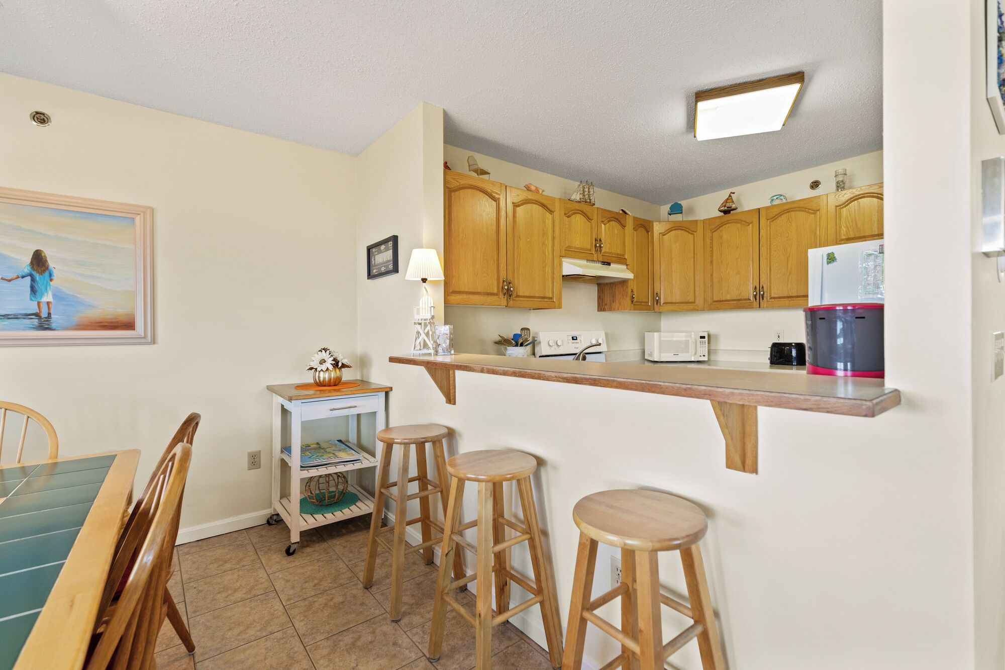 A compact kitchen with wooden cabinets, a microwave, a coffee maker, and a dining area with a table and chairs.