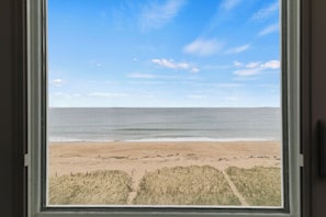Vista da praia através de uma janela com céu claro.