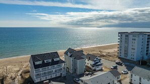 Una zona residencial costera con propiedades frente al mar, incluyendo un edificio de varios pisos con balcones y una casa independiente más pequeña con garaje.