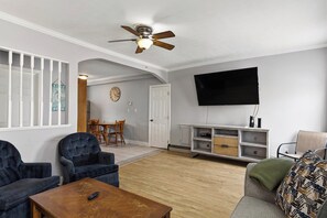 A living room with a ceiling fan, a flat-screen TV, a wooden dining table with chairs, and a sofa. - Seaside Village Condo #3- 300 ft to Sandy Beaches! (Old Orchard Beach)