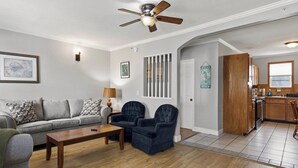 A living room with a sofa, two armchairs, a coffee table, a ceiling fan, and a kitchen area with wooden cabinets and a window. - Seaside Village Condo #3- 300 ft to Sandy Beaches! (Old Orchard Beach)