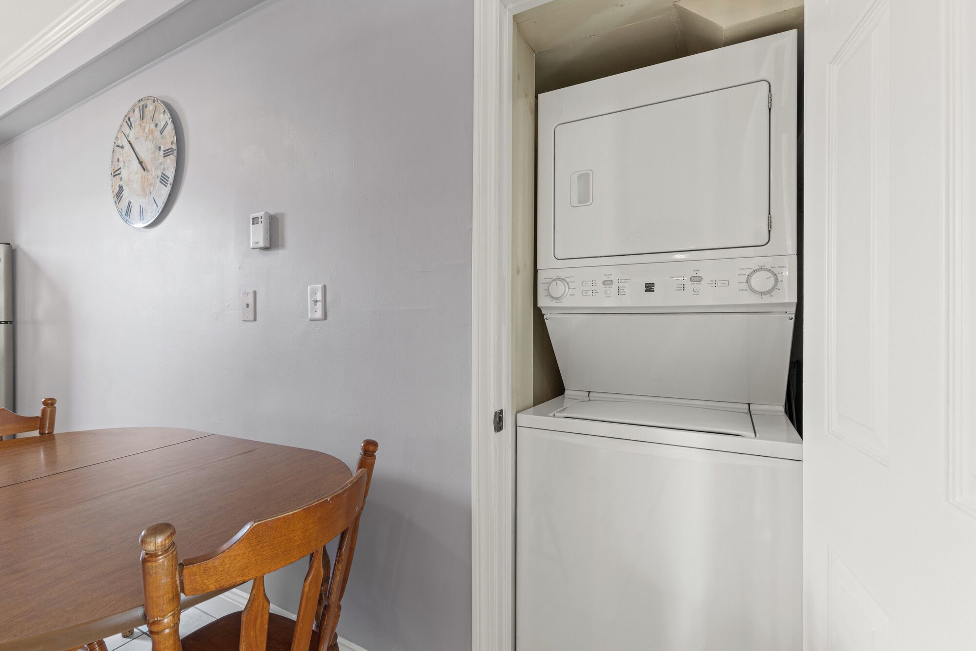 A compact laundry room with a built-in washer and dryer, a wooden dining table, and a wall clock.