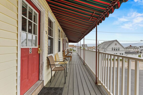 A wooden deck with a red door and a striped awning, overlooking a residential area.