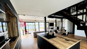 A modern kitchen with a large island, wooden flooring, and a view of the outdoors.