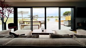 A modern room with a large sliding glass door leading to an outdoor deck with a view of a lake and distant landscape.