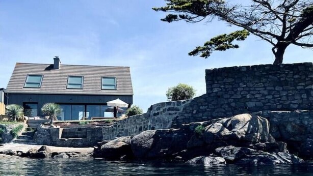 A modern house with a stone wall and a clear view of the water.
