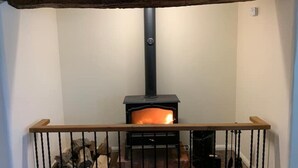 Una habitación con estufa de leña, baranda de madera y leña apilada.