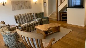 Una sala de estar con un sofá, sillones, una mesa de centro de madera y un televisor montado en la pared.