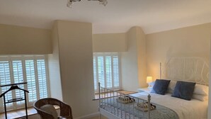 Un dormitorio con cama, una silla, una cuna y una ventana con persianas.
