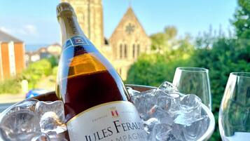 A bottle of Jules Ferraud Champagne in a bucket with ice cubes, with a glass and a wine glass nearby.