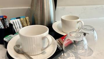 Una presentación para el desayuno con dos tazas blancas, una cuchara, un hervidor de té y una cafetera sobre una encimera.