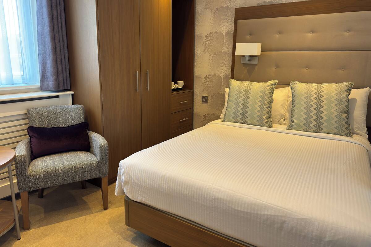 Une chambre d’hôtel avec un lit, une chaise, une armoire et une table de chevet.