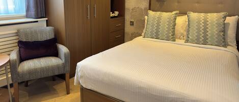 A hotel room with a bed, a chair, a wardrobe, and a nightstand.