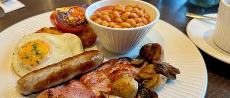 A plate of breakfast food including eggs, sausages, bacon, mushrooms, and baked beans.