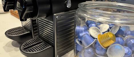A coffee machine with two drip trays and a jar filled with empty coffee cups.