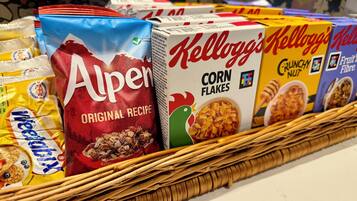 A variety of cereal boxes including Alpen, Kellogg's Corn Flakes, and Fruit'n Nut, arranged on a wicker tray.