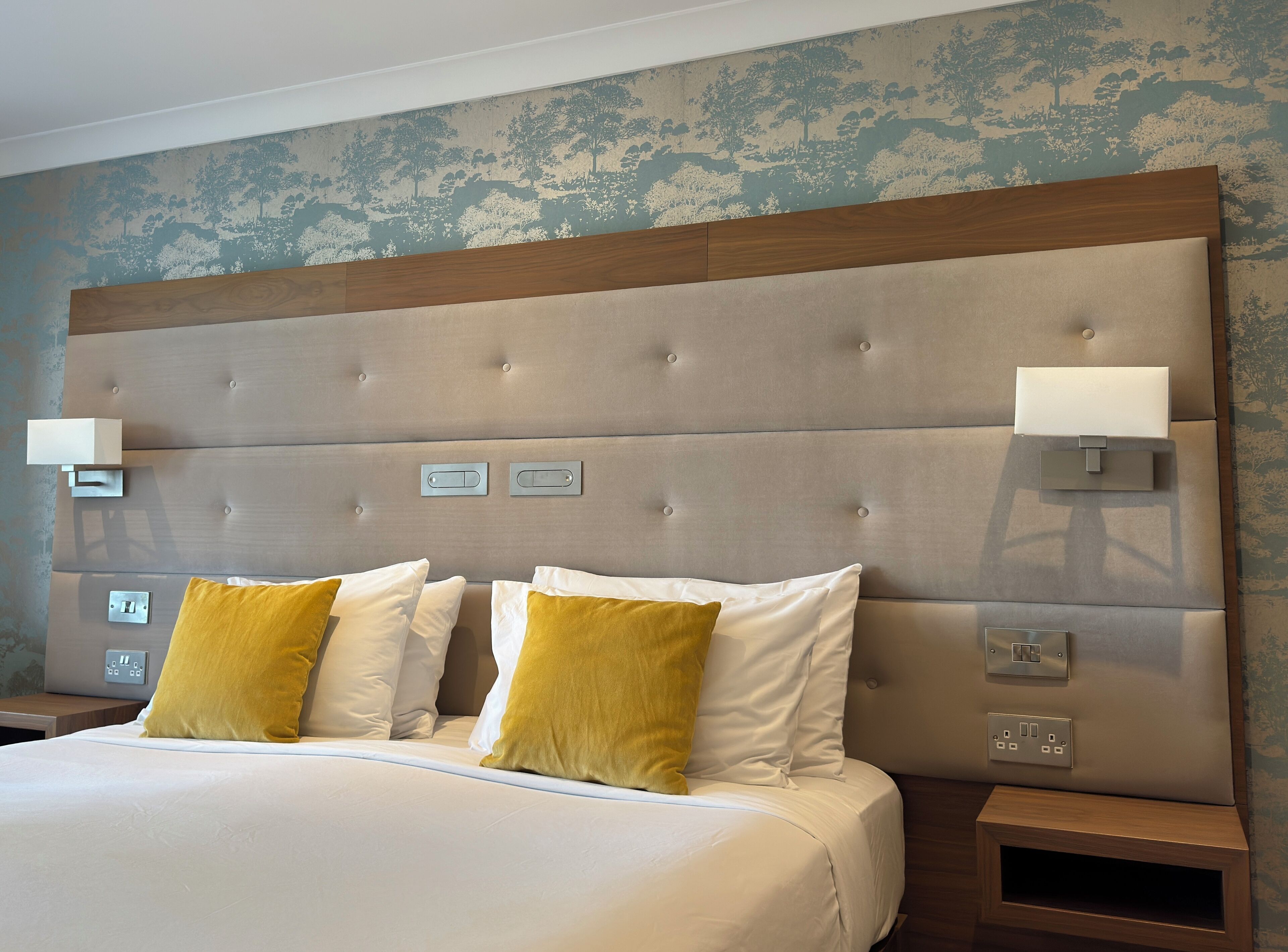 A hotel room with a large bed, two bedside lamps, and a nightstand with a power outlet.