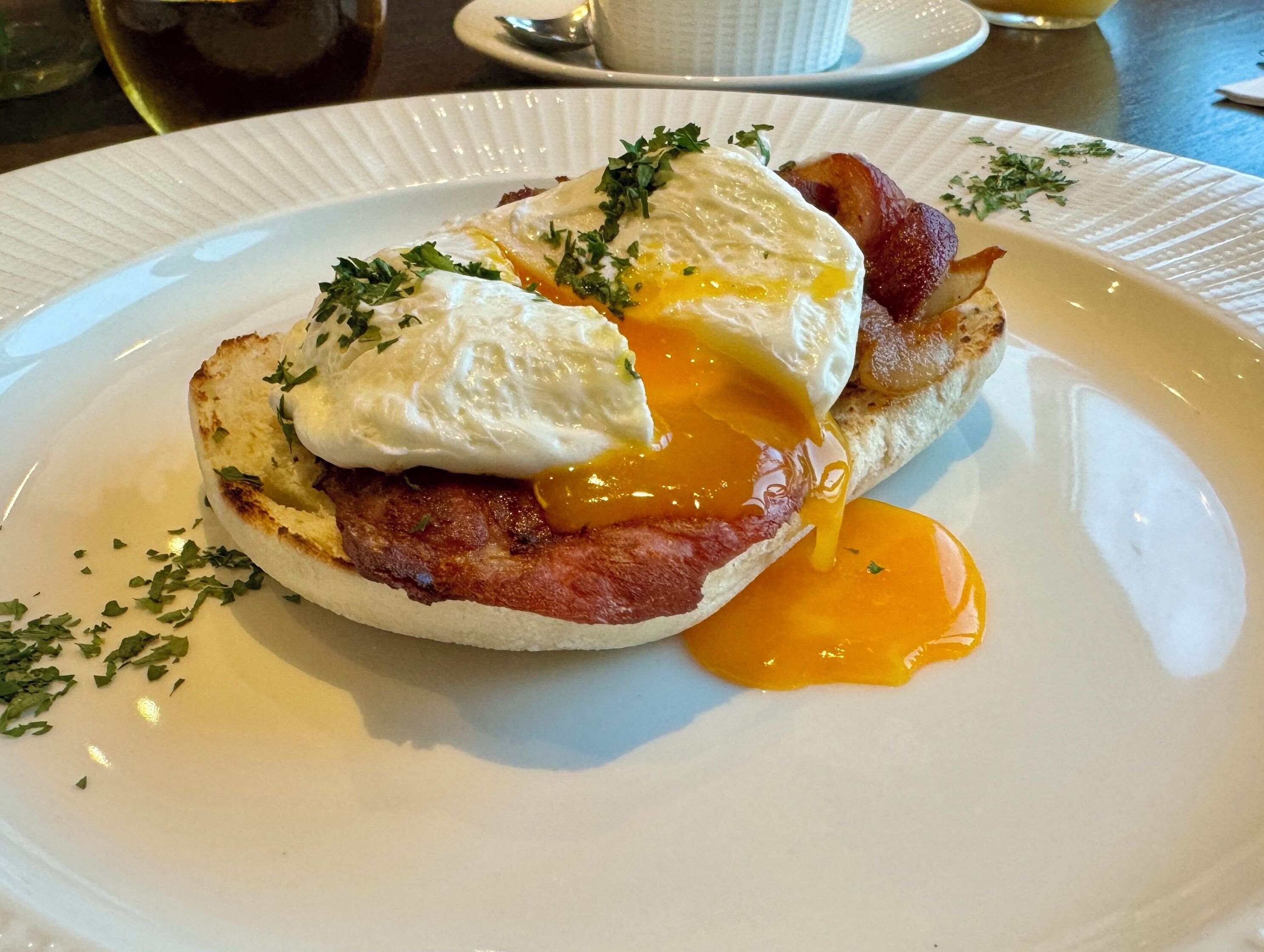 A plate with a breakfast dish consisting of a poached egg, bacon, and hollandaise sauce.