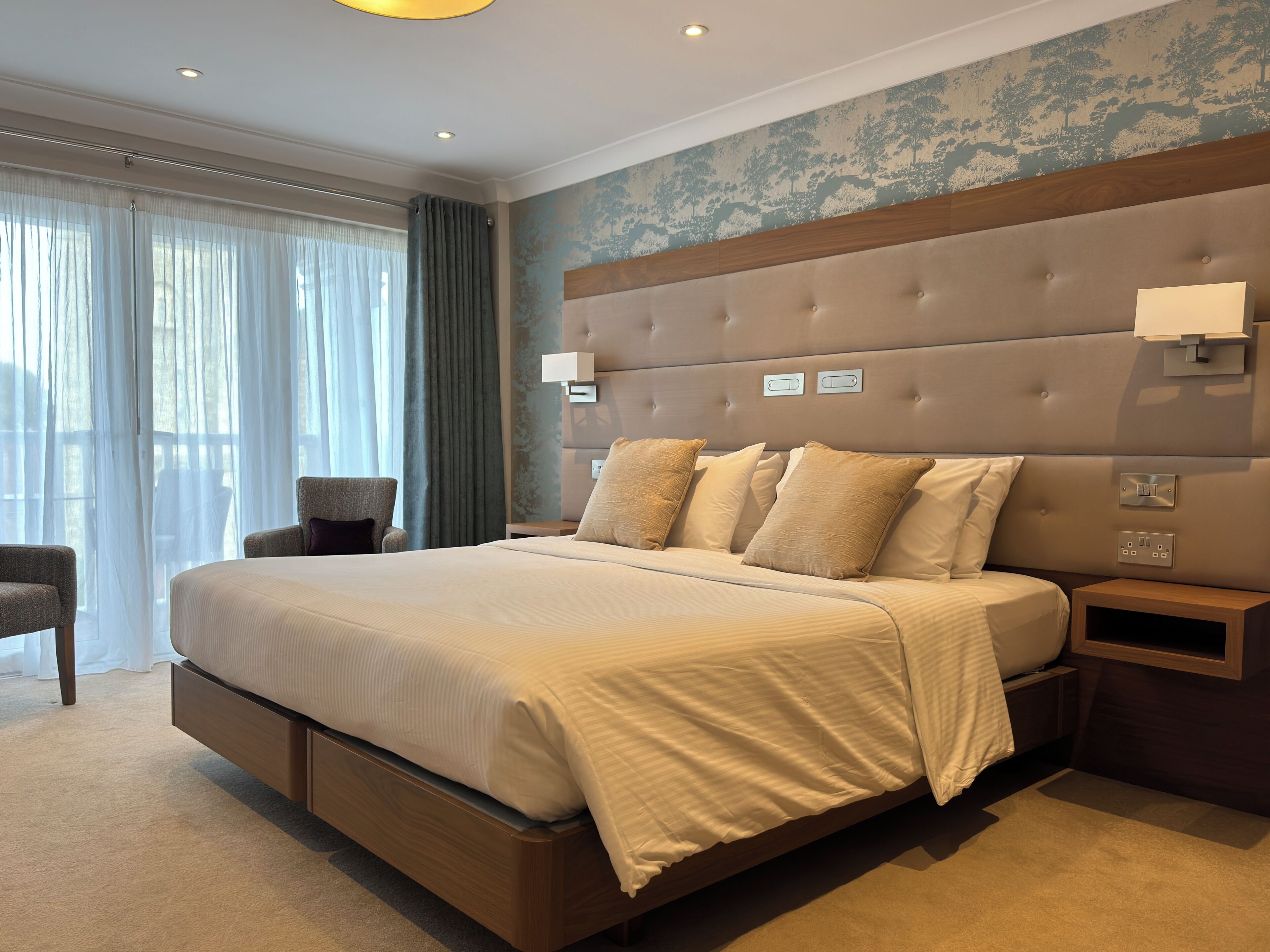 A modern hotel bedroom with a large bed, a nightstand, and a chair.