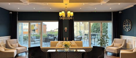 A hotel lobby with a central seating area, a chandelier, and a large window offering a view of the outside.