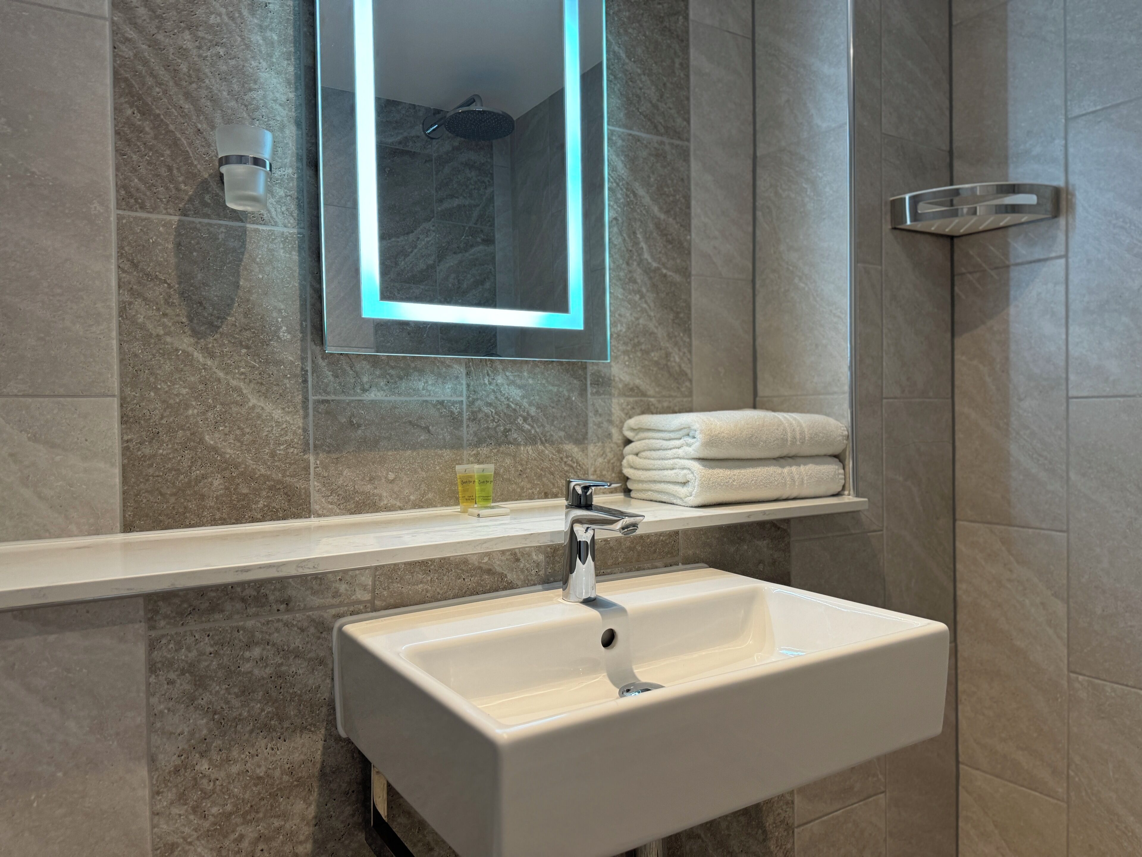 Een badkamer met een wit wastafelmeubel, een spiegel met verlichting en een handdoekhouder.